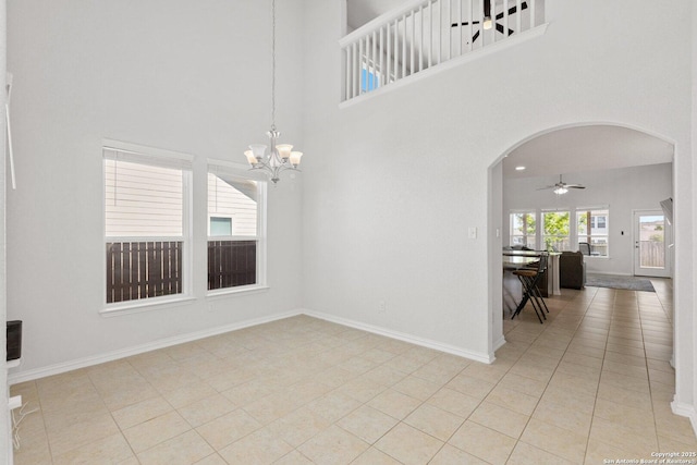 spare room with baseboards, arched walkways, a towering ceiling, and ceiling fan with notable chandelier