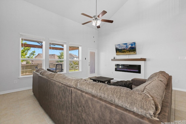 living area featuring a ceiling fan, light tile patterned floors, baseboards, a glass covered fireplace, and high vaulted ceiling