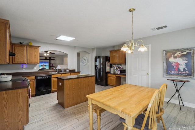 kitchen with dark countertops, a sink, arched walkways, a center island, and black appliances