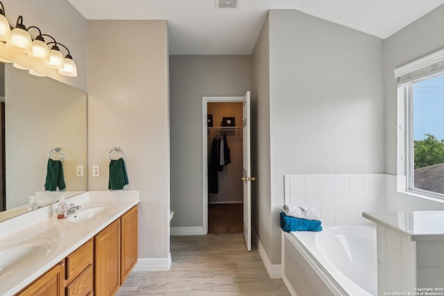 bathroom featuring a bath, wood finished floors, a sink, and double vanity