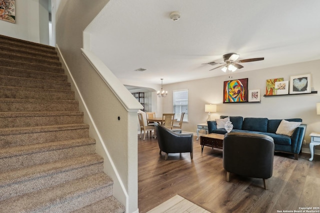 living area with wood finished floors, stairs, visible vents, and ceiling fan with notable chandelier