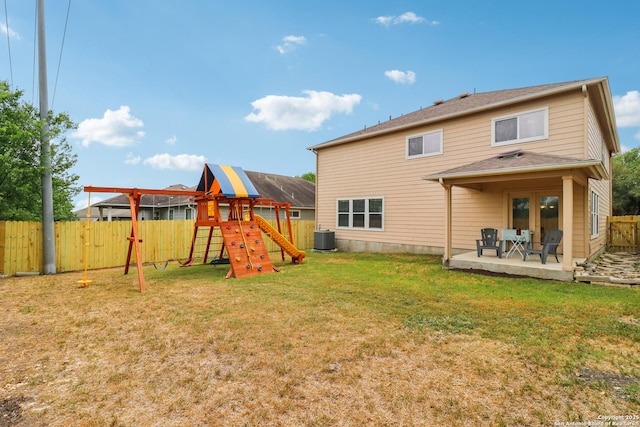 rear view of house featuring a lawn, central AC unit, a playground, and fence