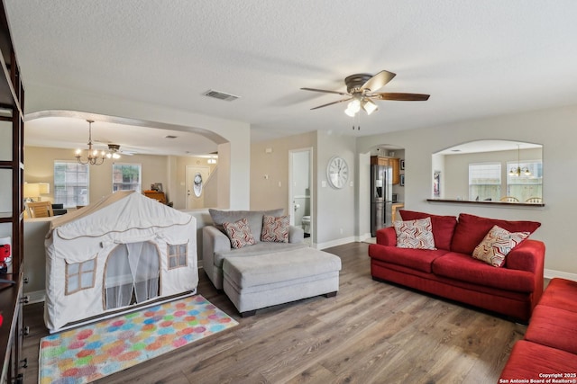 living room with wood finished floors, visible vents, arched walkways, baseboards, and ceiling fan with notable chandelier