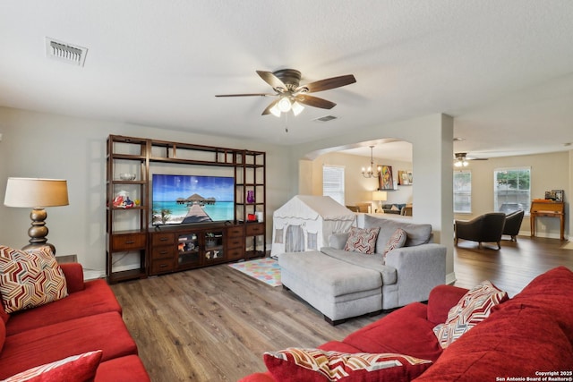 living area featuring ceiling fan with notable chandelier, wood finished floors, visible vents, and arched walkways