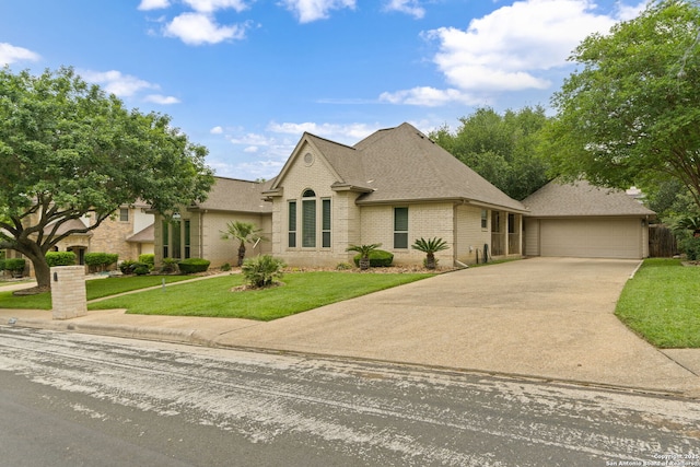 french country home featuring driveway, a front yard, a garage, brick siding, and roof with shingles
