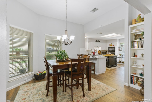 dining room with baseboards, light wood-style flooring, visible vents, and a notable chandelier