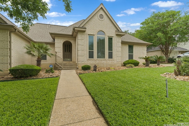french country home featuring brick siding, a shingled roof, and a front yard