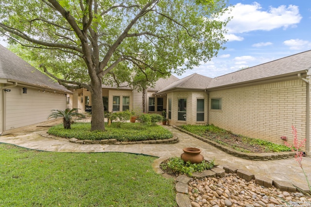 rear view of property featuring brick siding, a yard, and roof with shingles