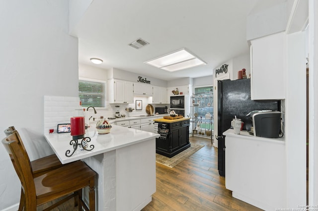 kitchen with a peninsula, light countertops, dark wood finished floors, backsplash, and visible vents