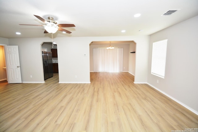 unfurnished living room with ceiling fan with notable chandelier, baseboards, visible vents, and arched walkways