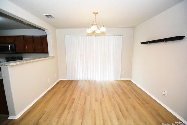 unfurnished dining area with light wood finished floors, baseboards, a notable chandelier, and visible vents