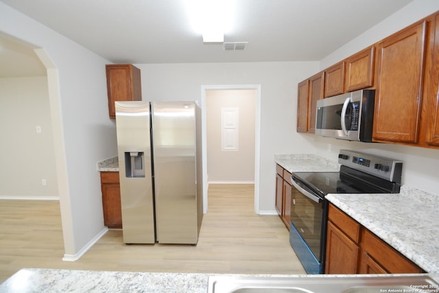 kitchen featuring brown cabinets, arched walkways, stainless steel appliances, light wood-style flooring, and baseboards