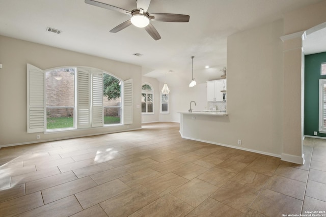 unfurnished living room with baseboards, ceiling fan, visible vents, and a sink