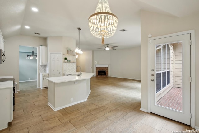 kitchen with a sink, a fireplace, ceiling fan with notable chandelier, white cabinetry, and visible vents