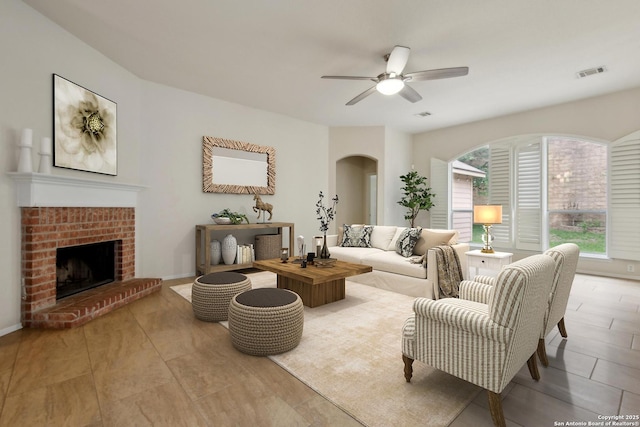 living room with a brick fireplace, a ceiling fan, arched walkways, and visible vents