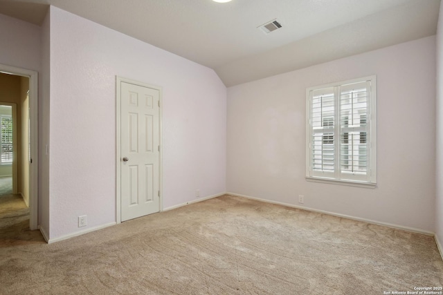 spare room featuring vaulted ceiling, baseboards, carpet flooring, and visible vents