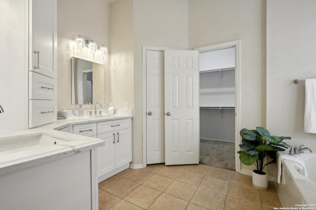 bathroom with a walk in closet, a garden tub, tile patterned floors, baseboards, and vanity