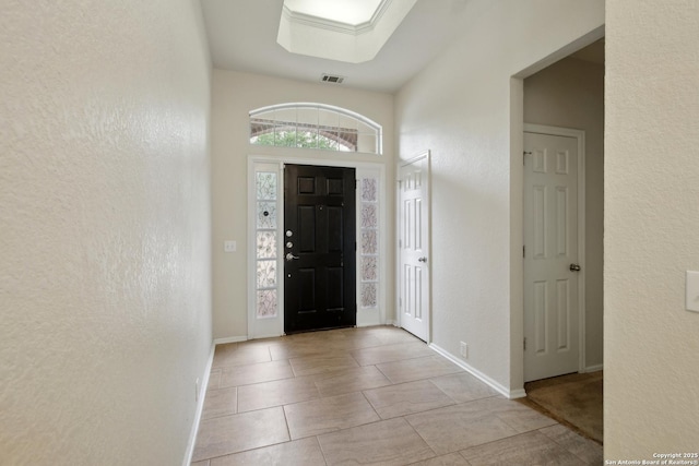 tiled entrance foyer featuring baseboards, a textured wall, and visible vents