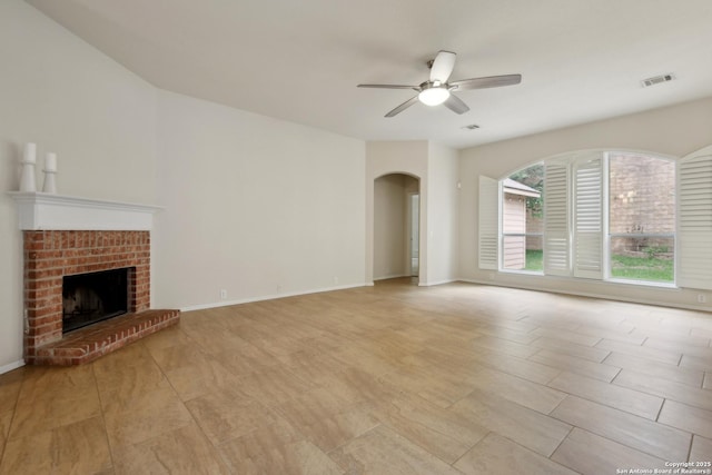 unfurnished living room with a ceiling fan, visible vents, arched walkways, a brick fireplace, and baseboards