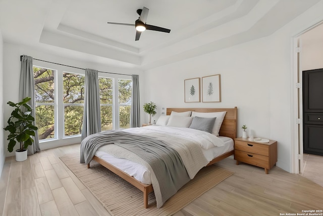bedroom featuring a ceiling fan, light wood-style floors, and a raised ceiling