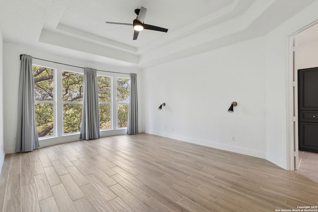 unfurnished room with baseboards, a tray ceiling, light wood-style floors, and ceiling fan
