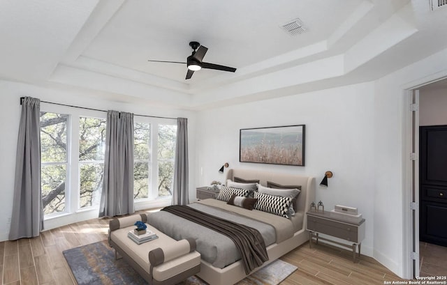 bedroom featuring a tray ceiling, visible vents, baseboards, a ceiling fan, and wood tiled floor