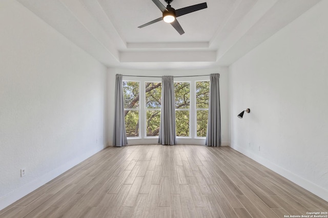 spare room with baseboards, wood finished floors, a tray ceiling, and ceiling fan