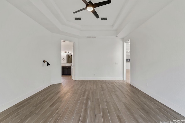 interior space with a raised ceiling, wood finished floors, visible vents, and ceiling fan