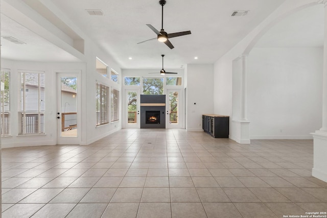 unfurnished living room with a warm lit fireplace, visible vents, a ceiling fan, light tile patterned flooring, and baseboards