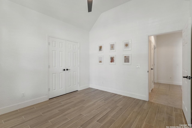 empty room with vaulted ceiling, a ceiling fan, baseboards, and light wood-type flooring