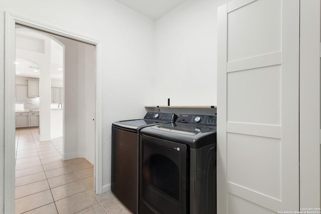washroom featuring arched walkways, washing machine and clothes dryer, light tile patterned floors, and laundry area