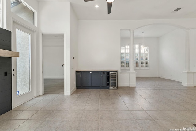 interior space with light tile patterned floors, ceiling fan, arched walkways, wine cooler, and decorative columns