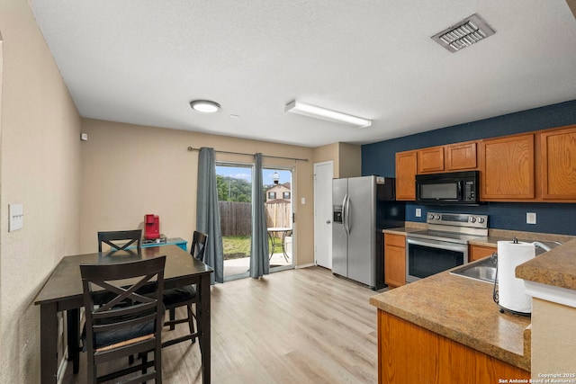 kitchen with light wood finished floors, brown cabinetry, visible vents, and appliances with stainless steel finishes