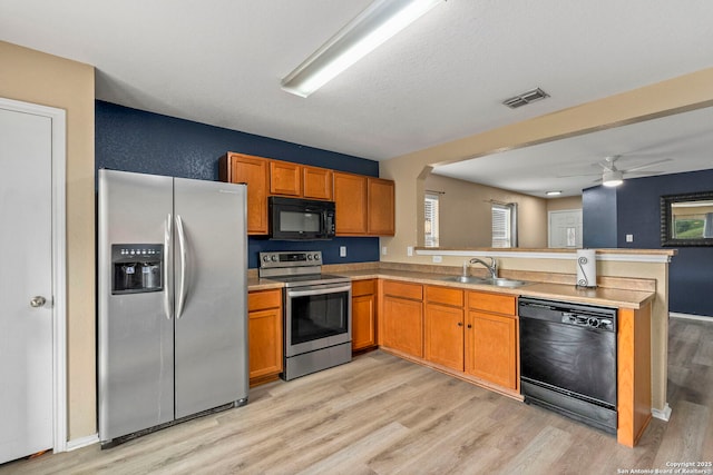 kitchen featuring a peninsula, a sink, light wood-style floors, brown cabinets, and black appliances