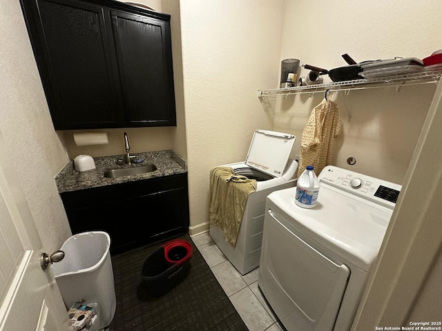 clothes washing area featuring a sink, washing machine and dryer, cabinet space, a textured wall, and light tile patterned floors