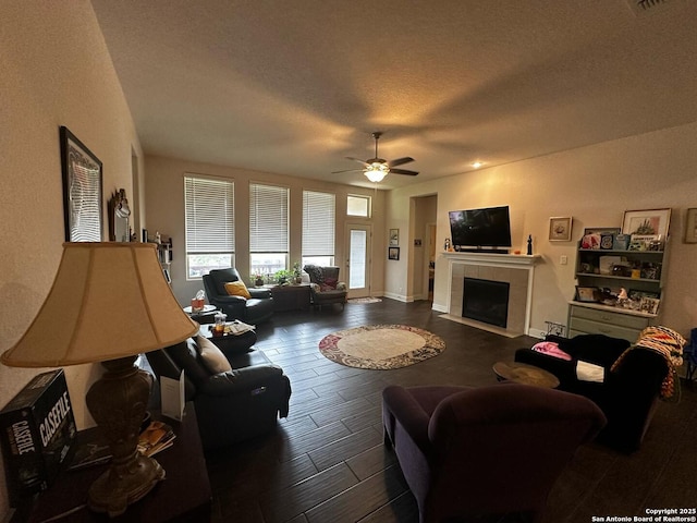 living room with a tile fireplace, ceiling fan, wood finished floors, and a textured ceiling