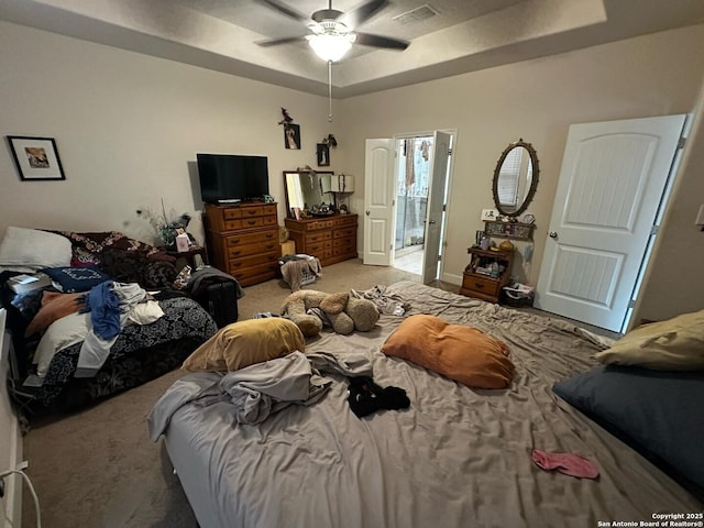 carpeted bedroom featuring ceiling fan, visible vents, and a raised ceiling