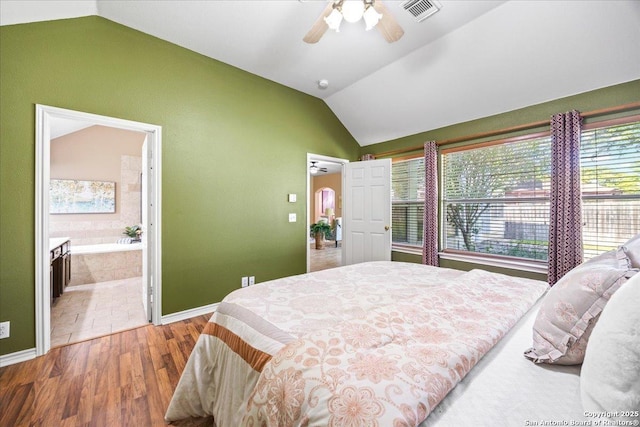 bedroom with vaulted ceiling, wood finished floors, baseboards, ensuite bath, and visible vents