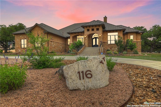 view of front of property with stone siding, a standing seam roof, a chimney, and metal roof
