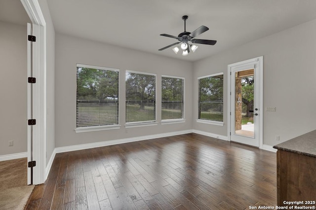 unfurnished room featuring a ceiling fan, baseboards, a wealth of natural light, and dark wood-style flooring