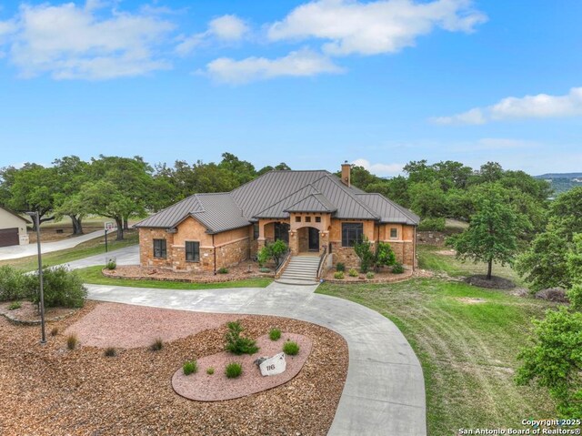view of front facade with a chimney, a front lawn, curved driveway, a standing seam roof, and metal roof