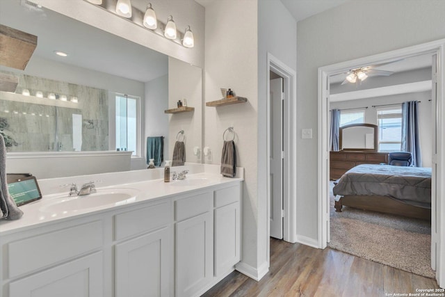 ensuite bathroom featuring wood finished floors, tiled shower, ceiling fan, and a sink