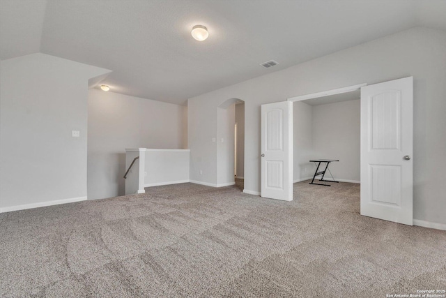 interior space featuring lofted ceiling, baseboards, carpet flooring, and arched walkways