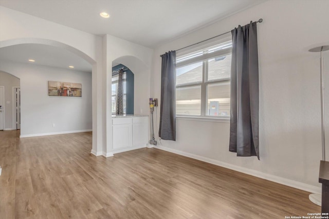 empty room featuring light wood finished floors, baseboards, and arched walkways
