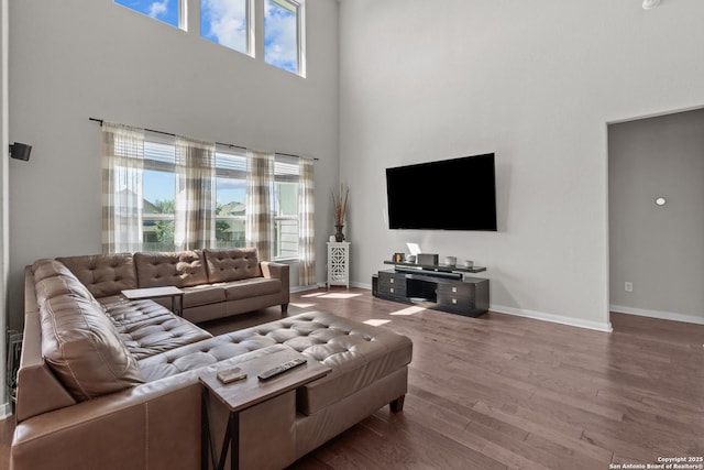 living area with baseboards, wood finished floors, and a towering ceiling