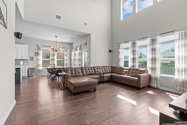 living area featuring dark wood finished floors, an inviting chandelier, a towering ceiling, and visible vents