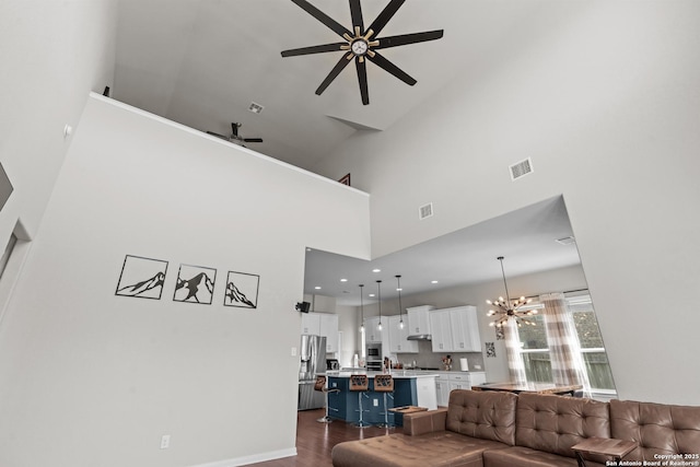 living area with dark wood-type flooring, visible vents, a high ceiling, and ceiling fan with notable chandelier