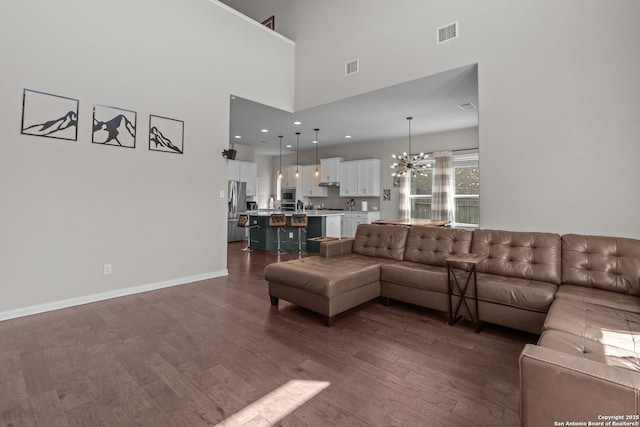 living room featuring dark wood-type flooring, visible vents, a notable chandelier, and a high ceiling