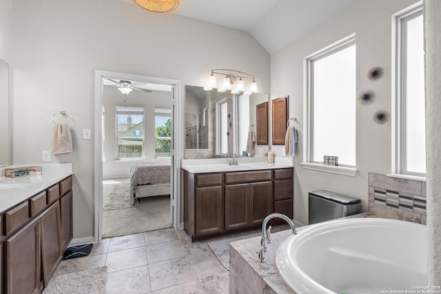 ensuite bathroom with a bath, vaulted ceiling, a wealth of natural light, and two vanities