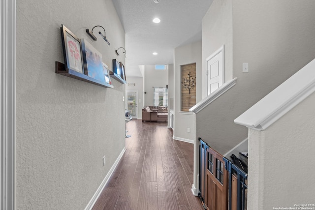corridor featuring a textured wall, baseboards, dark wood-style floors, and recessed lighting